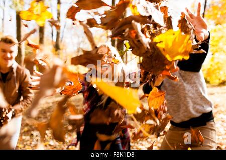 Junge Frau und zwei Teenager-Brüder werfen Herbstlaub im Wald Stockfoto