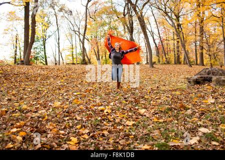 Junge Frau läuft und hält Decke im herbstlichen Wald Stockfoto