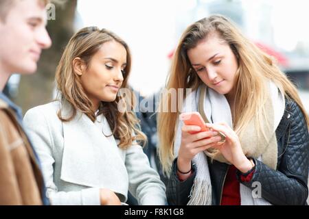 Junge Frau mit Freunden zu lesen unter Smartphone Texte auf Straße Stockfoto