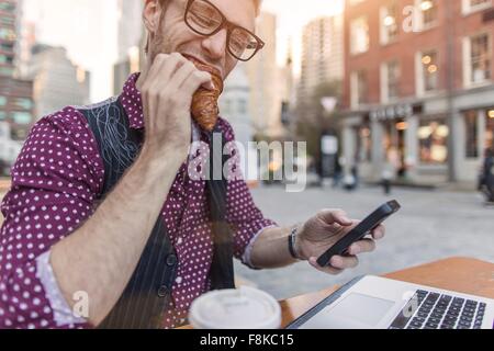 Betonte jungen Geschäftsmann Smartphone lesen, während des Essens im Straßencafé, New York, USA Stockfoto