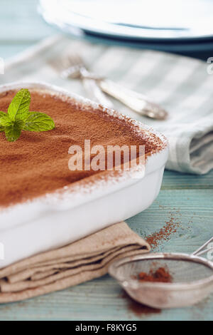 Tiramisu-Kuchen in einer Pfanne Ofen auf einem blauen Holztisch mit Gerichten und Gabeln Stockfoto