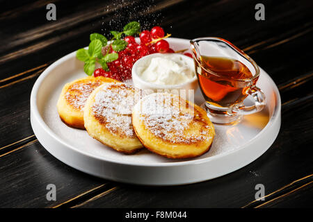 Braten, hausgemachter Hüttenkäse Pfannkuchen russische Syrniki mit roten Johannisbeeren auf weißen Teller Stockfoto