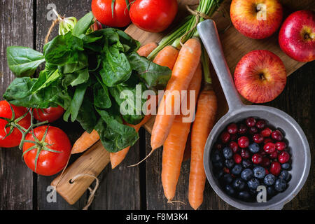 Auswahl an frischem Obst, Gemüse und Beeren. Reihe von Karotten, Spinat, Tomaten und rote Äpfel auf Schneidebrett, bluebe Stockfoto