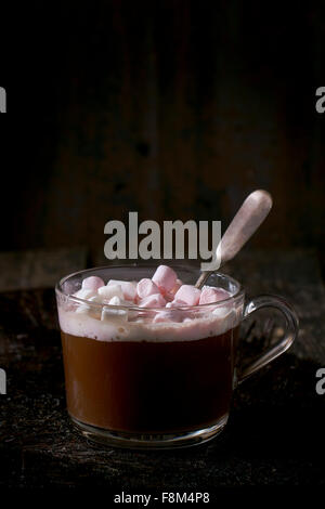 Glas-Tasse heiße Schokolade mit Marshmallows und Vintage Silber Löffel über alten Holztisch schmelzen. Dunkel rustikalen Stil. Stockfoto