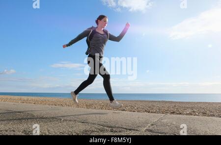 Junge Frau läuft weg am Kiesstrand Stockfoto