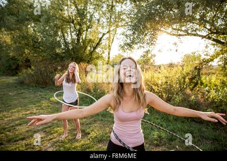 Zwei junge Mädchen in ländlicher Umgebung, herumalbern, mit Hula Hoops, Stockfoto