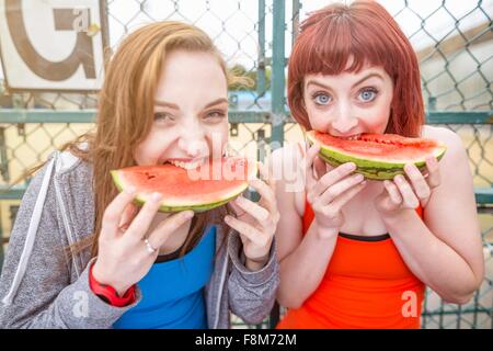 Junge Frauen Essen Wassermelone neben Sportplatz, London, UK Stockfoto