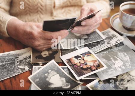 Ältere Frau sitzt am Tisch, Blick durch alte Fotografien, Mittelteil Stockfoto