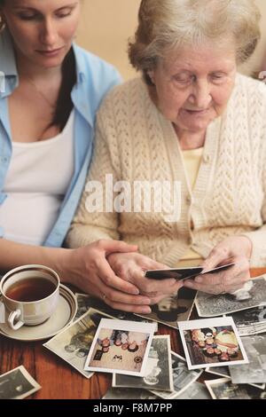 Ältere Frau und Enkelin sitzen am Tisch, Blick durch alte Fotografien Stockfoto