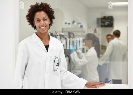 Wissenschaftler, die lächelnd im Labor, im Hintergrund arbeitenden Kolleginnen und Kollegen Stockfoto