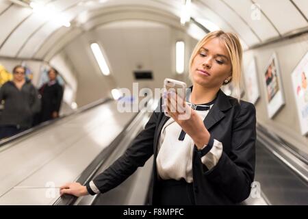 Geschäftsfrau SMS auf Rolltreppe, London Underground, UK Stockfoto