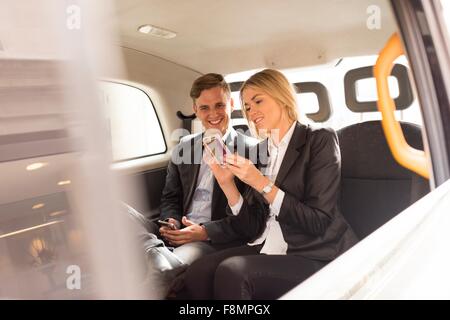 Unternehmer und Unternehmerin mit Smartphone in schwarzen Taxi, London, UK Stockfoto