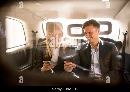 Unternehmer und Unternehmerin mit Smartphone in schwarzen Taxi, London, UK Stockfoto