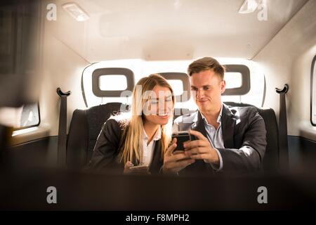 Unternehmer und Unternehmerin mit Smartphone in schwarzen Taxi, London, UK Stockfoto