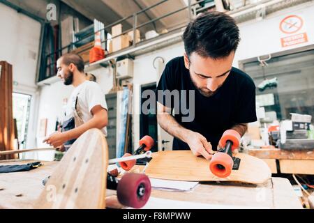 Junger Mann in Tischlerei Befestigung Räder Skateboard Stockfoto