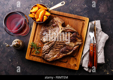 Mittlere seltene gegrilltes t-Bonesteak mit Kartoffelspalten und Wein servieren Board Block auf dunklem Hintergrund Stockfoto