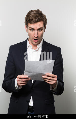 Blonden europäischen Geschäftsmann mit einem Angst Blick starrt auf ein Stück Papier mit schlechten Nachrichten drauf während vor einer Steigung Stockfoto