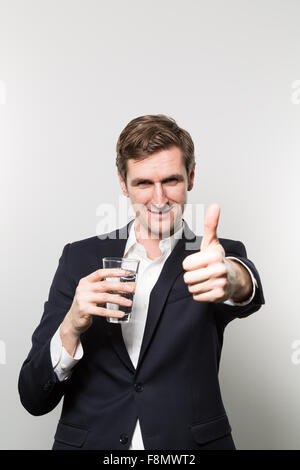 Blonden europäischen Geschäftsmann hält ein Glas Mineralwasser und gibt eine Schläge direkt auf die Kamera vor einem g Stockfoto