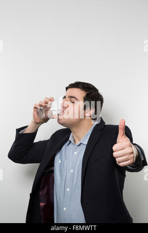 Dunkelhaarige Europäische Geschäftsmann mit einem frechen Look gibt einen klopft-Up beim Trinken aus einem Glas Wasser in der anderen Hand während Stockfoto