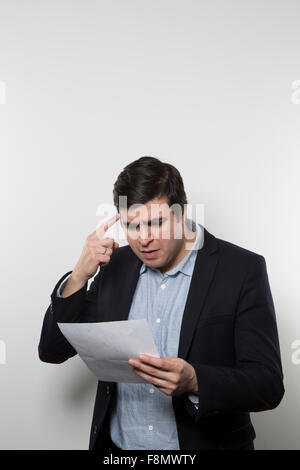 Dunkelhaarige Europäische Geschäftsmann mit einem Ungläubigen Blick starrt auf ein Stück Papier und hält seinen Zeigefinger an die Stirn w Stockfoto