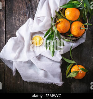 Schüssel mit Mandarinen mit Blättern und trockenen geschnittenen Orange auf weißem Textil Lappen über alten Holztisch. Stockfoto