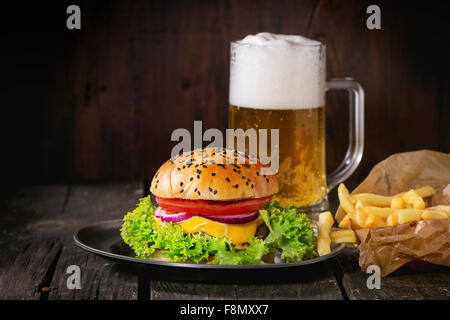 Frische hausgemachte Burger mit in alten Metall-Teller mit Pommes frites in Backpapier, serviert mit Glas kaltes Lager Bier über alte Stockfoto