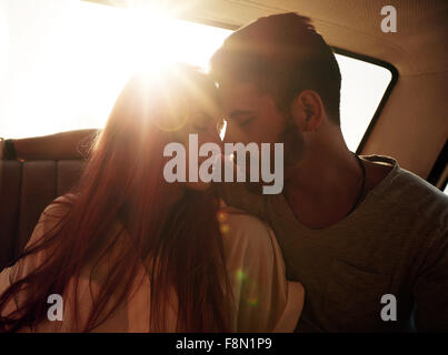Romantische junges Paar sitzt im hinteren Sitz eines Autos. Junges Paar Gefühl romantischen Platz auf der Rückseite eines Fahrzeugs mit Sonne Flare aus Stockfoto