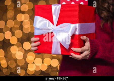 Roten Geschenkbox mit weißen Band holded von jungen Frau in Strickpullover über glitzernden Hintergrund Stockfoto