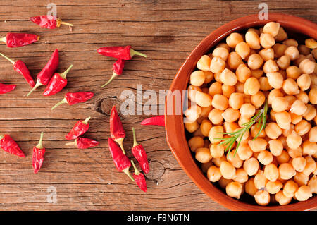 High-Angle Shot von einem Steingut-Schüssel mit gekochten Kichererbsen und einige rote Chilischoten auf einem rustikalen Holztisch Stockfoto