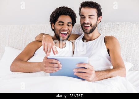 Glückliches schwules Paar mit Tablet auf Bett Stockfoto