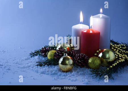 Leuchtenden weißen und roten Weihnachtskerzen, Goldene Kugeln, Tannenzweigen und Zapfen im Schnee auf einem hellblauen Hintergrund Stockfoto