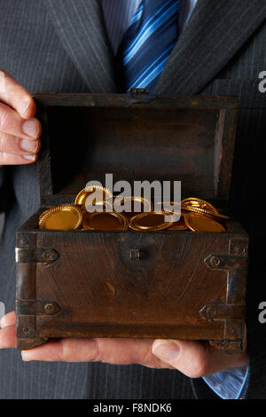 Geschäftsmann hält hölzerne Truhe mit Goldmünzen im Inneren Stockfoto