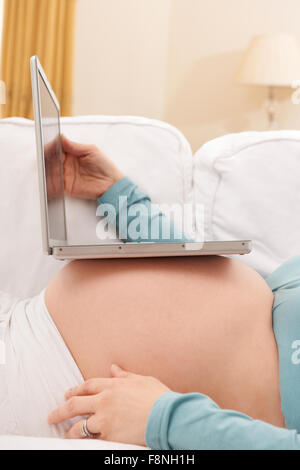 Schwangere Frau mit Laptop-Computer, die auf Bauch Stockfoto