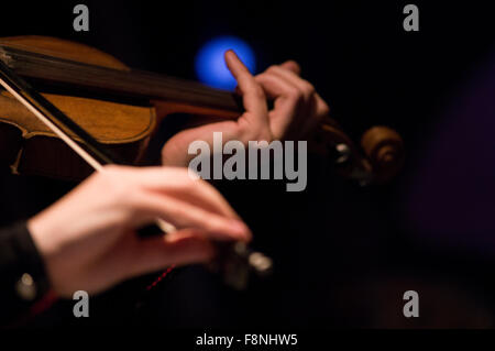 Hände spielen eine Geige mit einem blauen Scheinwerfer leuchten im Hintergrund Stockfoto