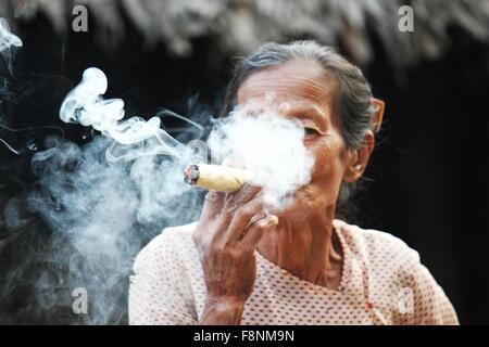 Lächelnde asiatische Frau raucht eine Zigarre Aufnahme in einem kleinen Dorf in der Nähe von Heide, in Myanmar Burma, wo eine Frau Zigarren b tut Stockfoto