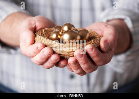 Mann hält Nest voller goldenen Eiern Stockfoto