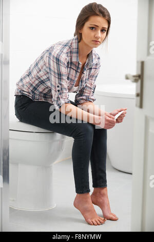 Teenager-Mädchen sitzen im Badezimmer mit Schwangerschaftstest Stockfoto