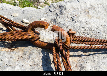 Verrostete eisernen Reifen, montiert auf Kalkstein Block mit alten rostigen Eisen Kabel um ihn herum geschlungen. Stockfoto