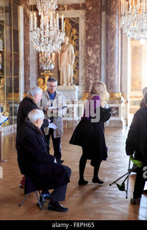 Ältere französische Touristen sitzen auf tragbaren Hocker beim Anhören von Tourguide in den Spiegelsaal im Schloss Versailles, Stockfoto