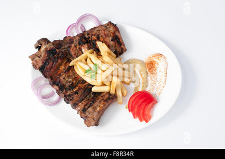 Gegrillte würzige Schweinerippchen garniert mit Pommes frites, rohen Zwiebelringen, Tomatenscheiben und ein wenig Senf auf ein Jota in Nahaufnahme Stockfoto