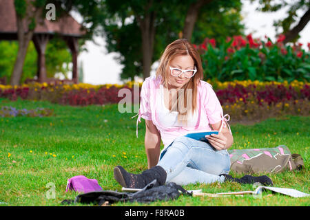 Junge Schülerin oder Studentin lernen und sitzen im Park auf dem grünen Rasen Stockfoto