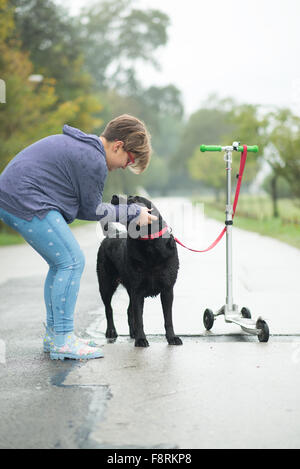 Mädchen streicheln Hund gebunden, Roller schieben Stockfoto