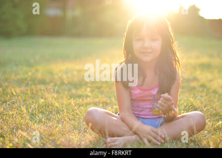 Porträt eines Mädchens Schneidersitz sitzen auf Rasen mit Sonne auf ihr Haar Stockfoto