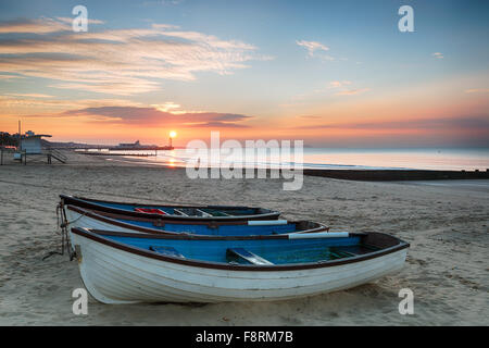 Atemberaubenden Sonnenaufgang Ove Rfishing Boote bei Durley Chine am Strand von Bournemouth in Dorset mit die Sonne über das Ende des Piers Stockfoto