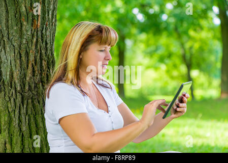 Porträt einer Frau 50 Jahre alt mit einem Tablet in der Hand im park Stockfoto