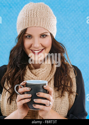 Foto von einem schönen Brünette eingehüllt in warme Schal und Mütze, eine heißen Kaffee oder heiße Schokolade zu trinken. Stockfoto