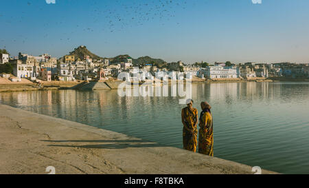 Hindu-Pilger ist als Kulisse für ein Bad im Heiligen See in der Dämmerung mit Häusern und Hügeln ankommen. Stockfoto