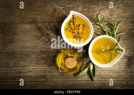 Olivenöl mit frischen Kräutern auf hölzernen Hintergrund. Stockfoto