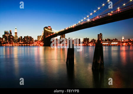 Skyline von New York City Manhattan mit Brooklyn Bridge und Büro Wolkenkratzern, die Gebäude in der Dämmerung, bei Nacht mit Lichtern beleuchtet Stockfoto