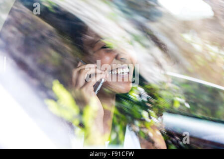 Eine attraktive gemischten Rennen junge Frau in einem Auto plaudern auf ihr Mobiltelefon als Passagier Stockfoto